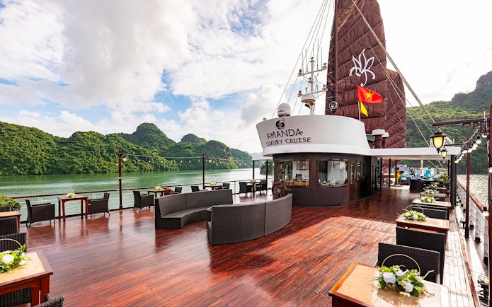 Public deck area on Amanda Luxury Cruise with seating and scenic views of lush green hills.