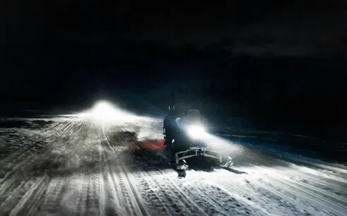 Snowmobile on snowy trail at night during Rovaniemi Northern Lights safari.