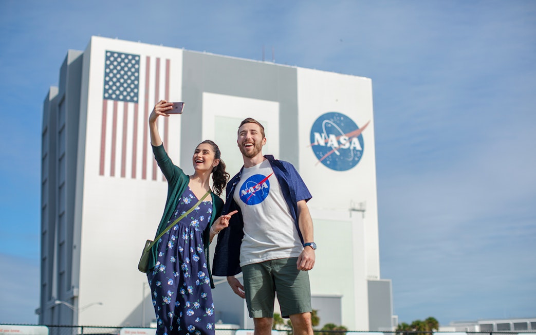 Visitors taking a selfie at Kennedy Space Center with NASA building in the background.