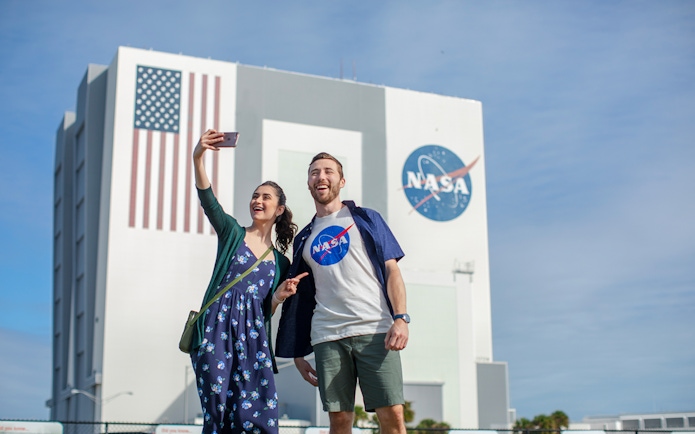Visitors taking a selfie at Kennedy Space Center with NASA building in the background.