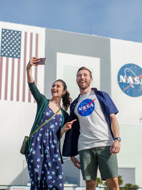 Visitors taking a selfie at Kennedy Space Center with NASA building in the background.