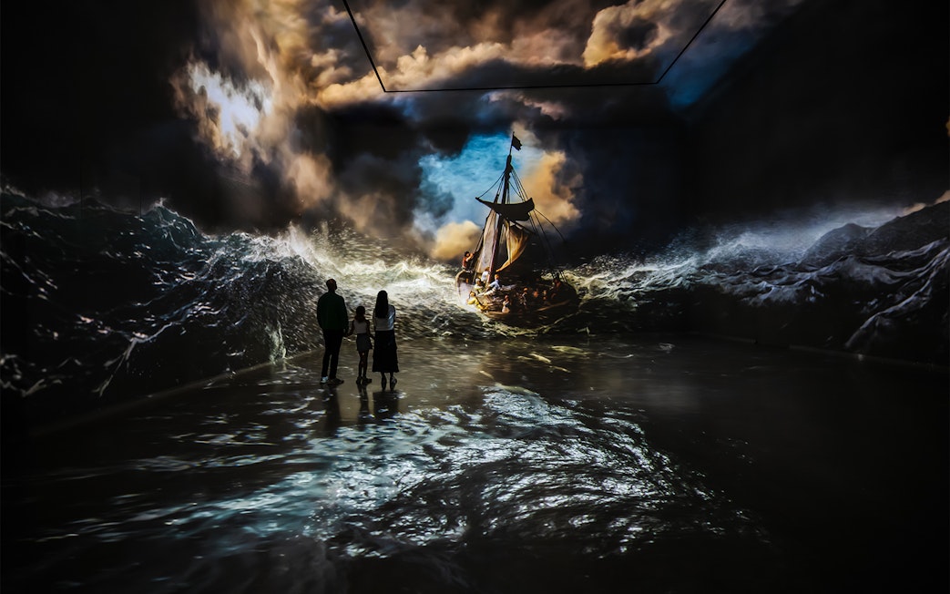 Visitors viewing immersive stormy sea art at Frameless London exhibit.