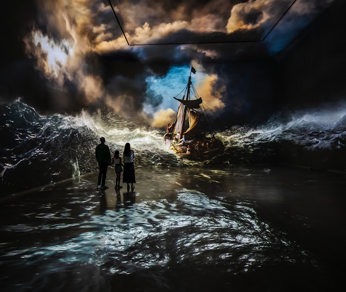 Visitors viewing immersive stormy sea art at Frameless London exhibit.