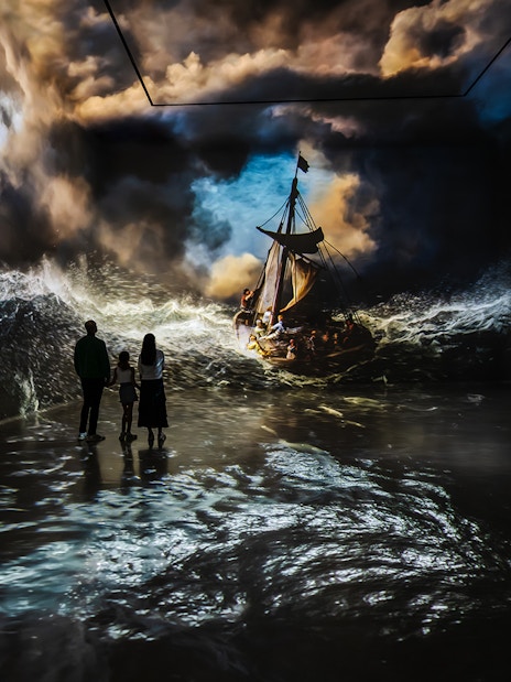 Visitors viewing immersive stormy sea art at Frameless London exhibit.