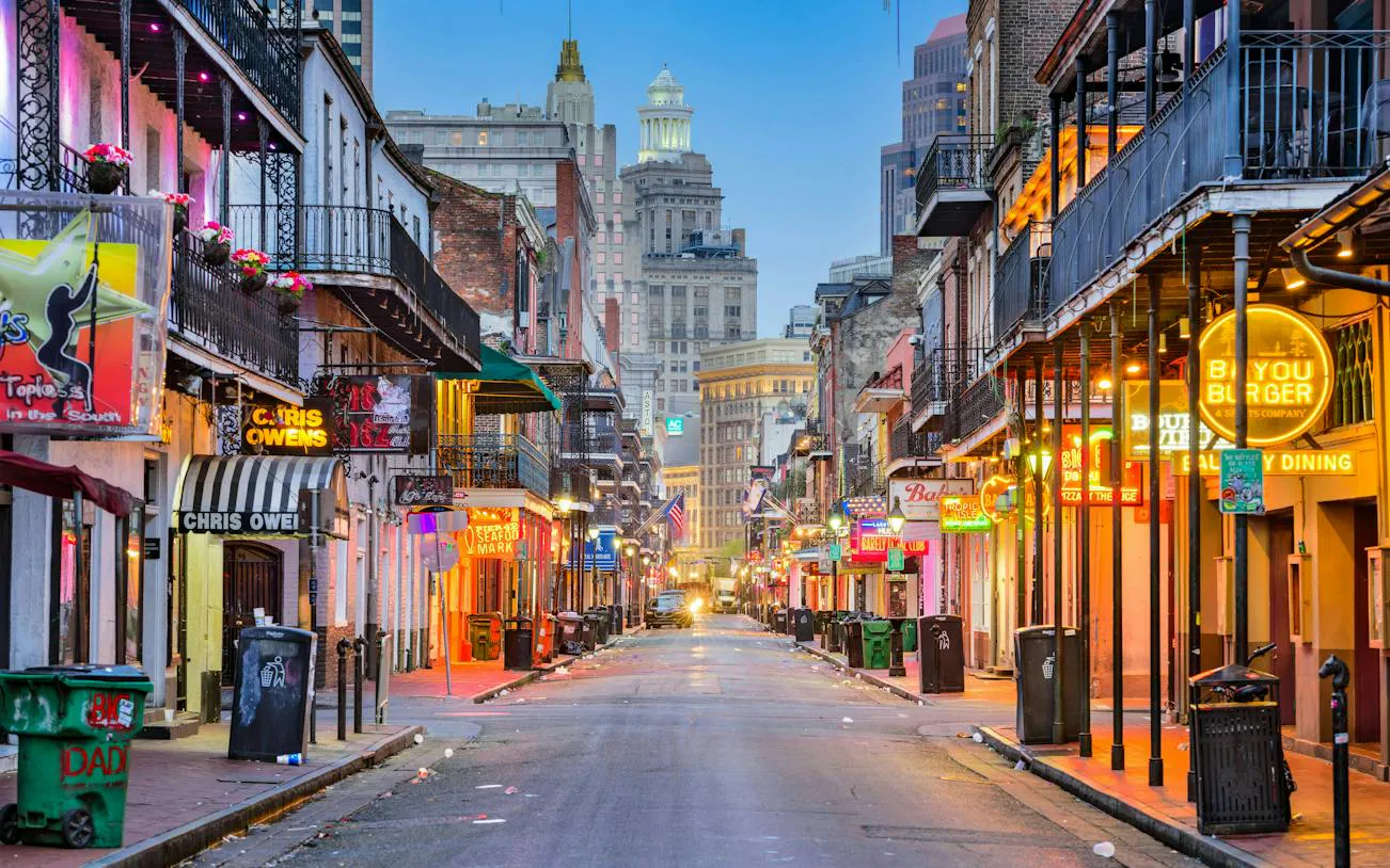 Bourbon Street in New Orleans with neon signs and historic buildings at dusk.