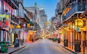 Bourbon Street in New Orleans with neon signs and historic buildings at dusk.