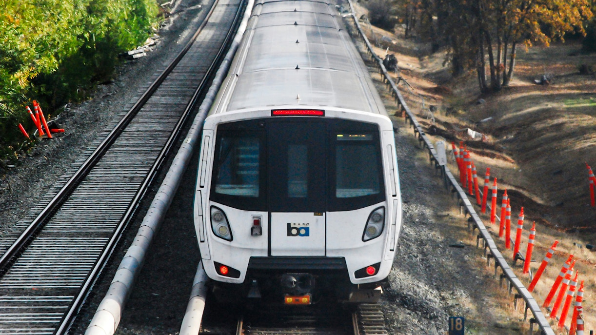 Bay Area Rapid Transit train on tracks surrounded by trees and construction cones.