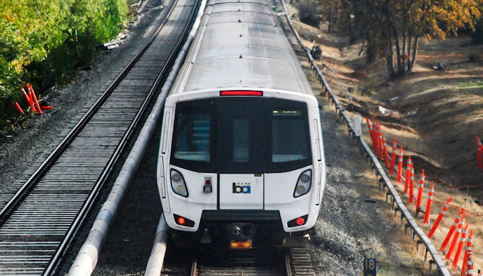 Bay Area Rapid Transit train on tracks surrounded by trees and construction cones.