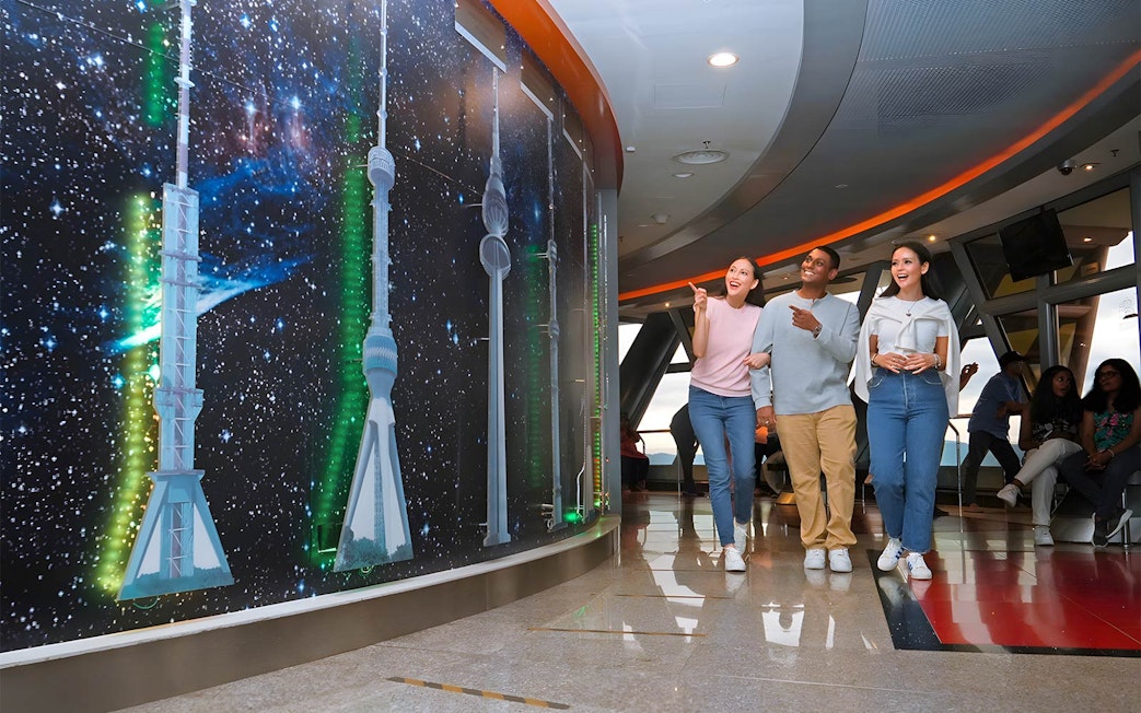 Visitors exploring KL Tower's Sky Deck with tower models and starry backdrop.