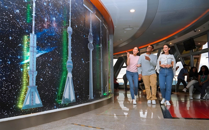 Visitors exploring KL Tower's Sky Deck with tower models and starry backdrop.