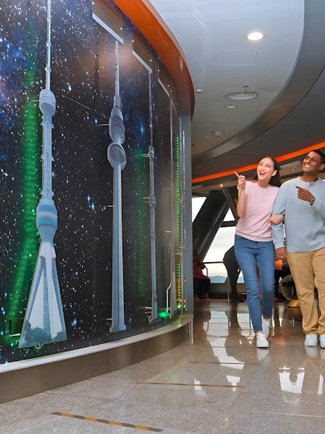 Visitors exploring KL Tower's Sky Deck with tower models and starry backdrop.