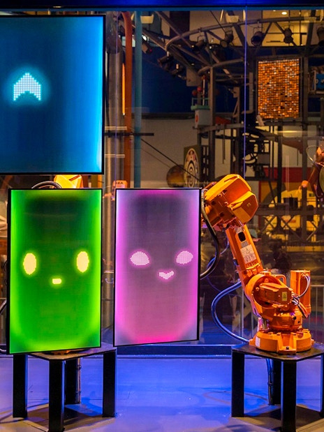 Interactive robot exhibit at Science Centre Singapore with digital screens and robotic arms.