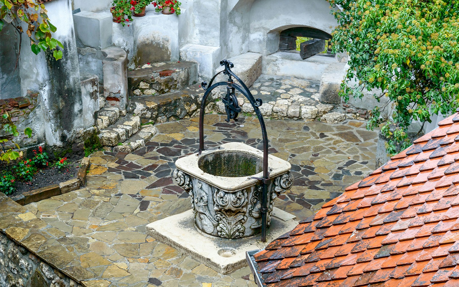 Courtyard well at Bran Castle, Romania, surrounded by stone walls and red-tiled roof.