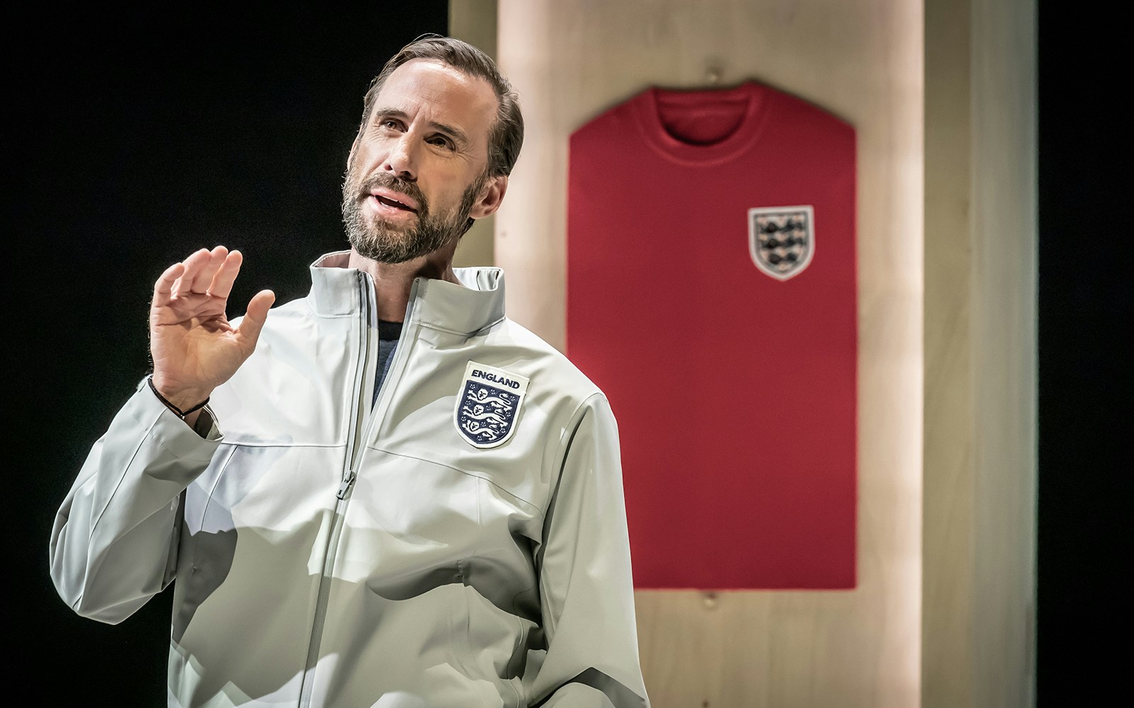 Man in England jacket speaking with red England jersey in background.