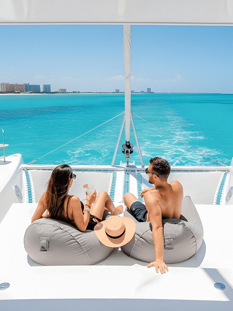 Tourists relaxing with drinks on a catamaran in Isla Mujeres, turquoise sea in background.