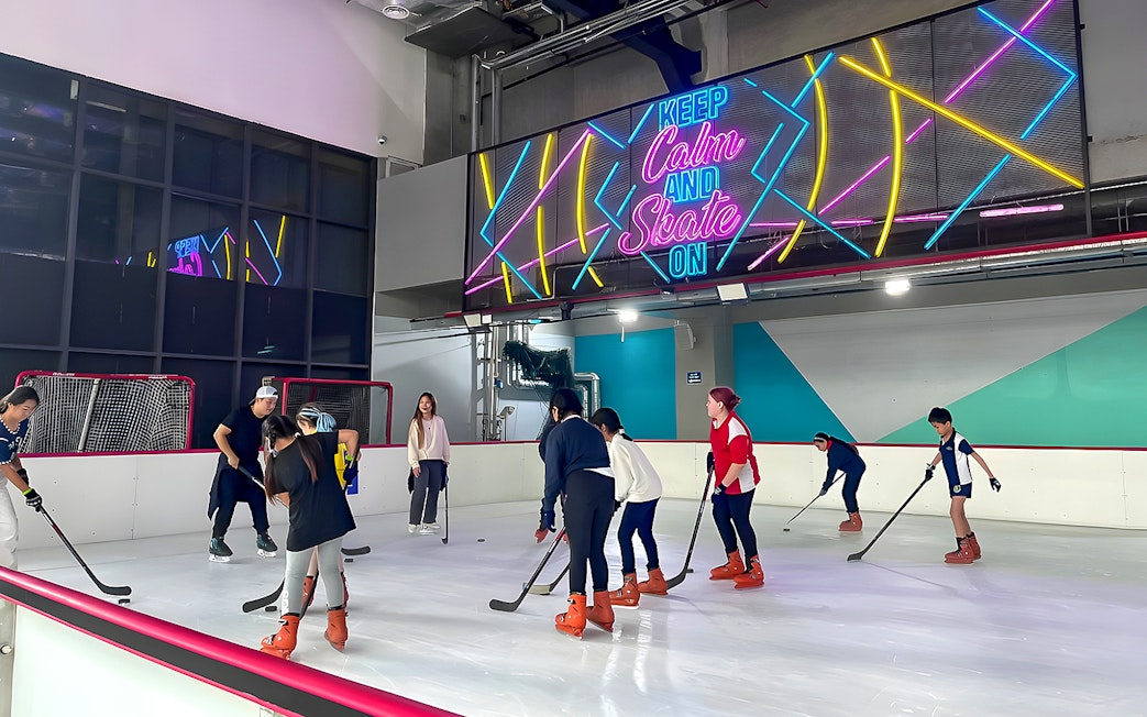 Ice skaters playing hockey at Blue Ice Snow Park, 163 Retail Park, under neon sign.
