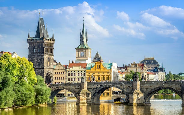 Charles Bridge over Vltava River in Prague with historic towers and buildings in the background.