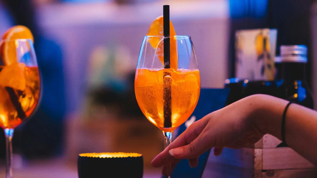 Hand holding a cocktail glass with orange slices on a pizza cruise.