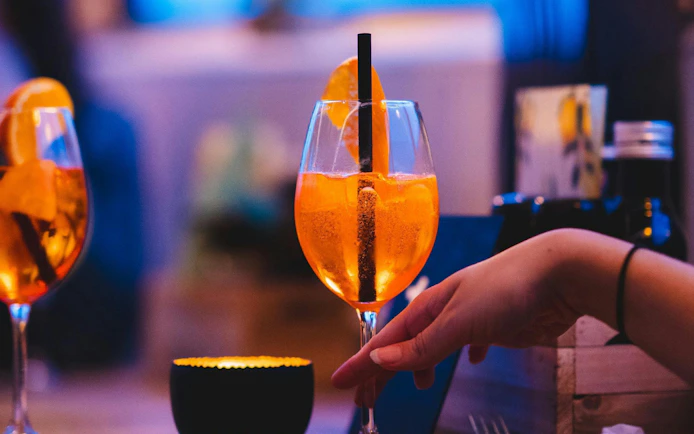 Hand holding a cocktail glass with orange slices on a pizza cruise.