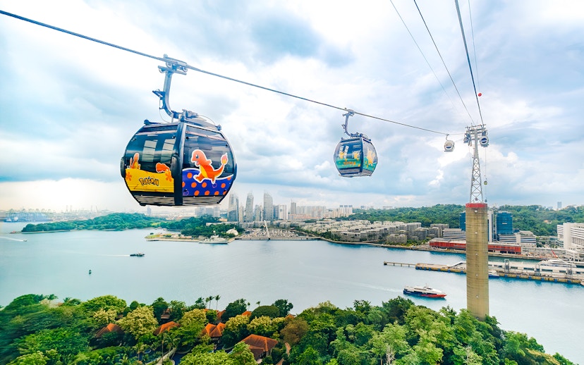 Cable car with Pokémon theme over Sentosa, Singapore, with city skyline and water view.