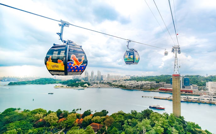 Cable car with Pokémon theme over Sentosa, Singapore, with city skyline and water view.
