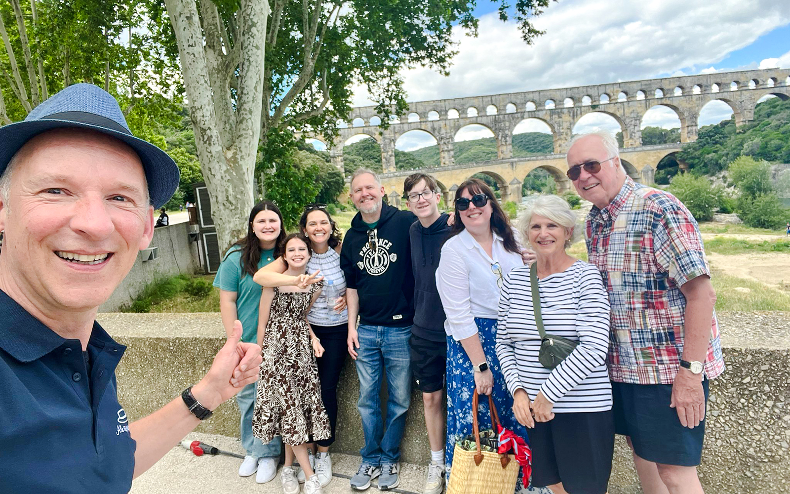 Group of tourists smiling in front of Pont du Gard, France.