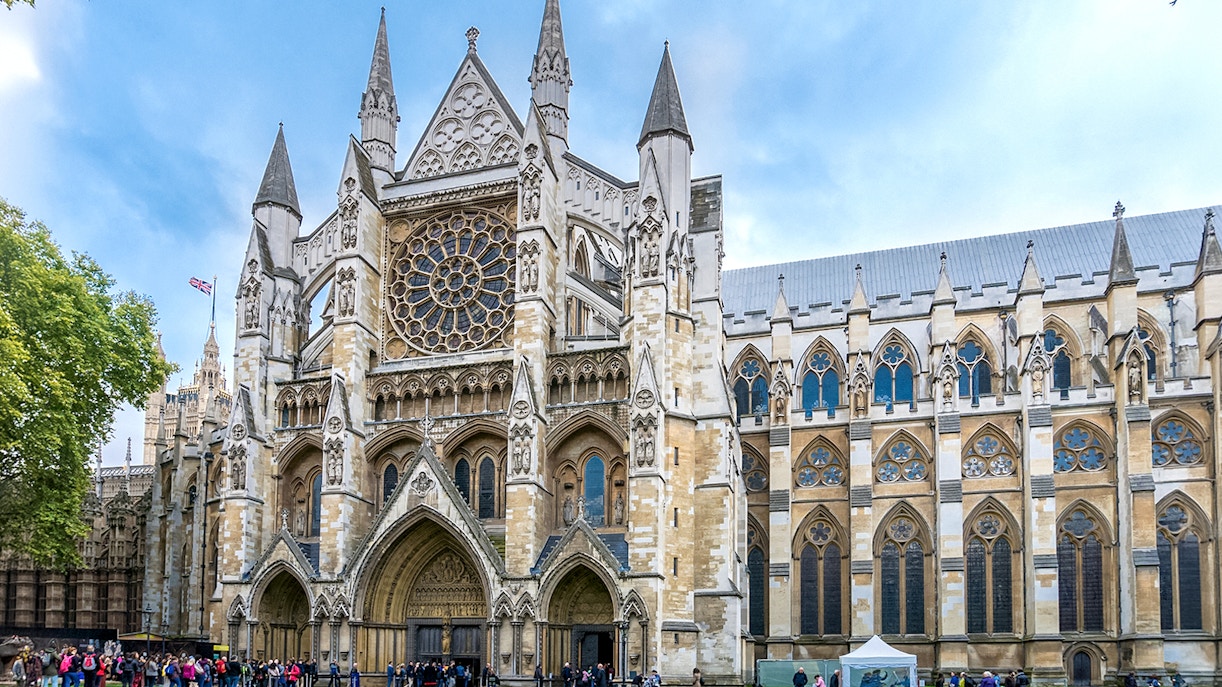 Westminster Abbey façade with rose window and tourists in London.