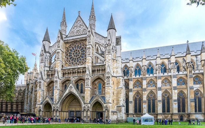 Westminster Abbey façade with rose window and tourists in London.