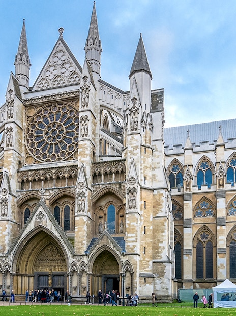 Westminster Abbey façade with rose window and tourists in London.