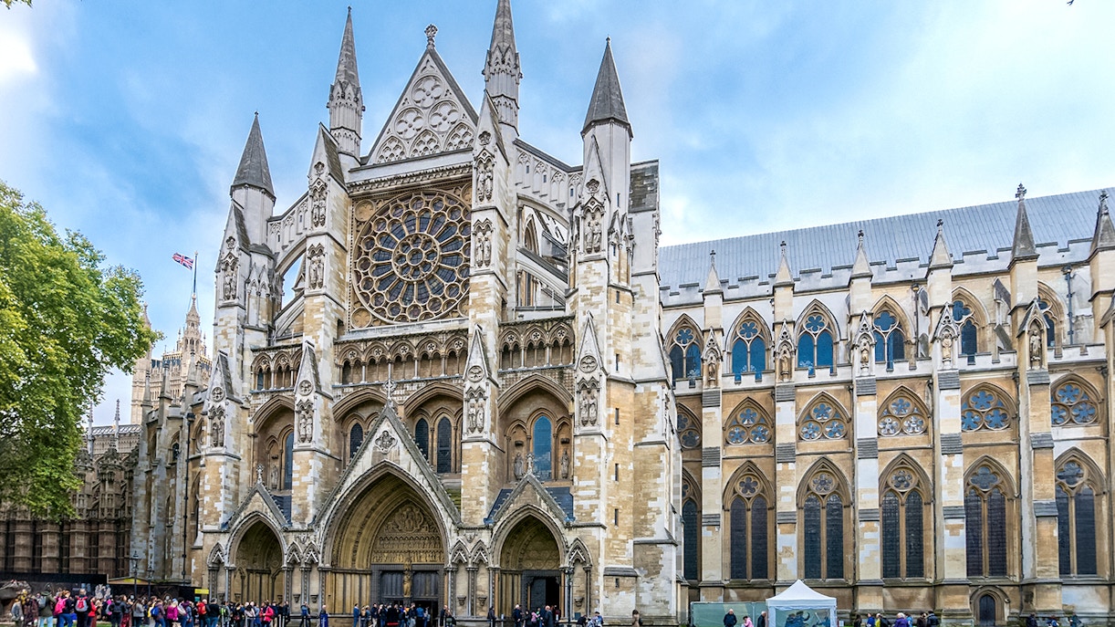 Westminster Abbey façade with rose window and tourists in London.