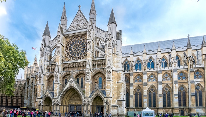 Westminster Abbey façade with rose window and tourists in London.