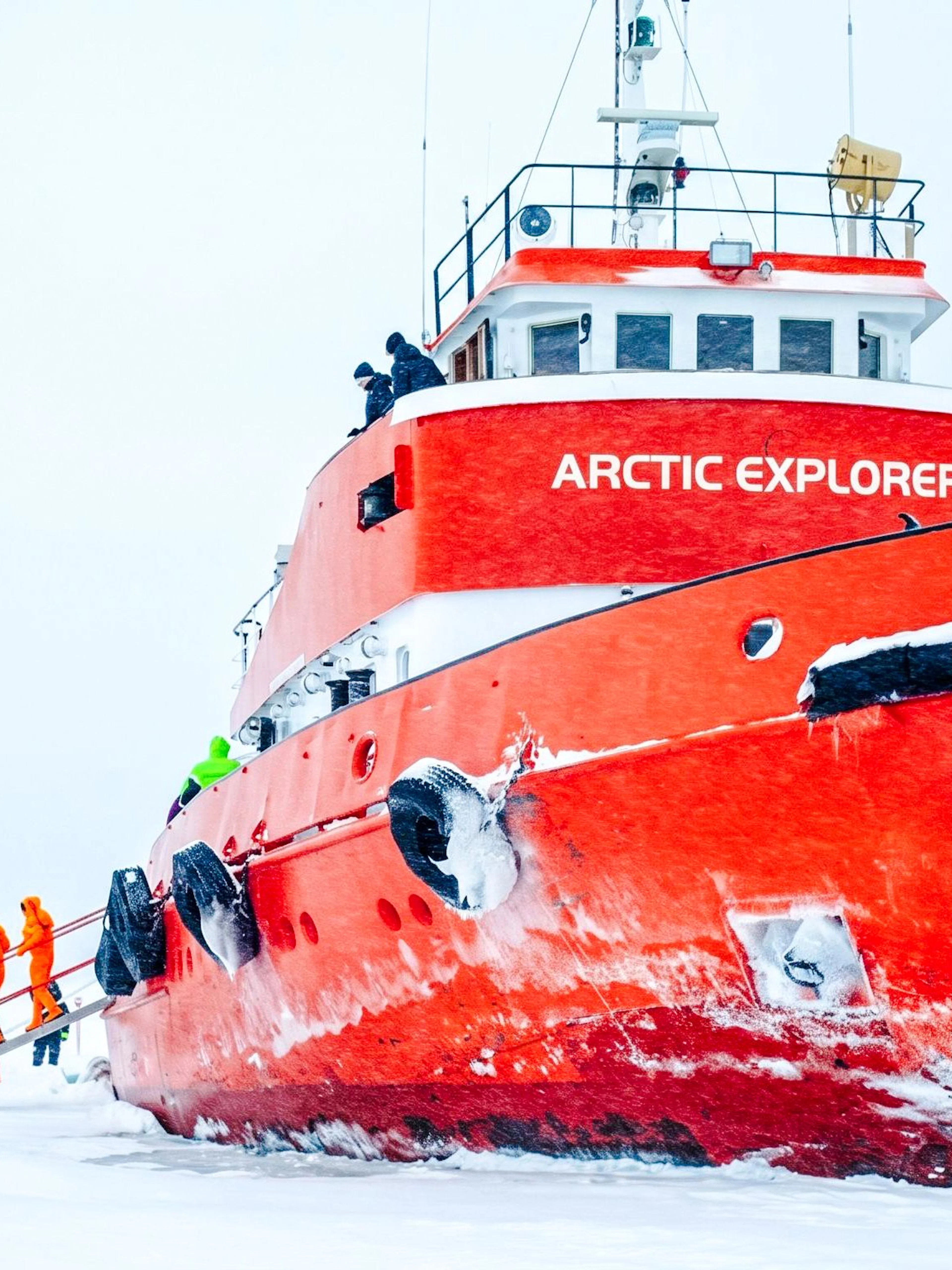 Icebreaker cruise ship in icy waters with passengers in orange suits.