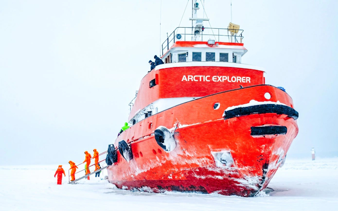 Icebreaker cruise ship in icy waters with passengers in orange suits.