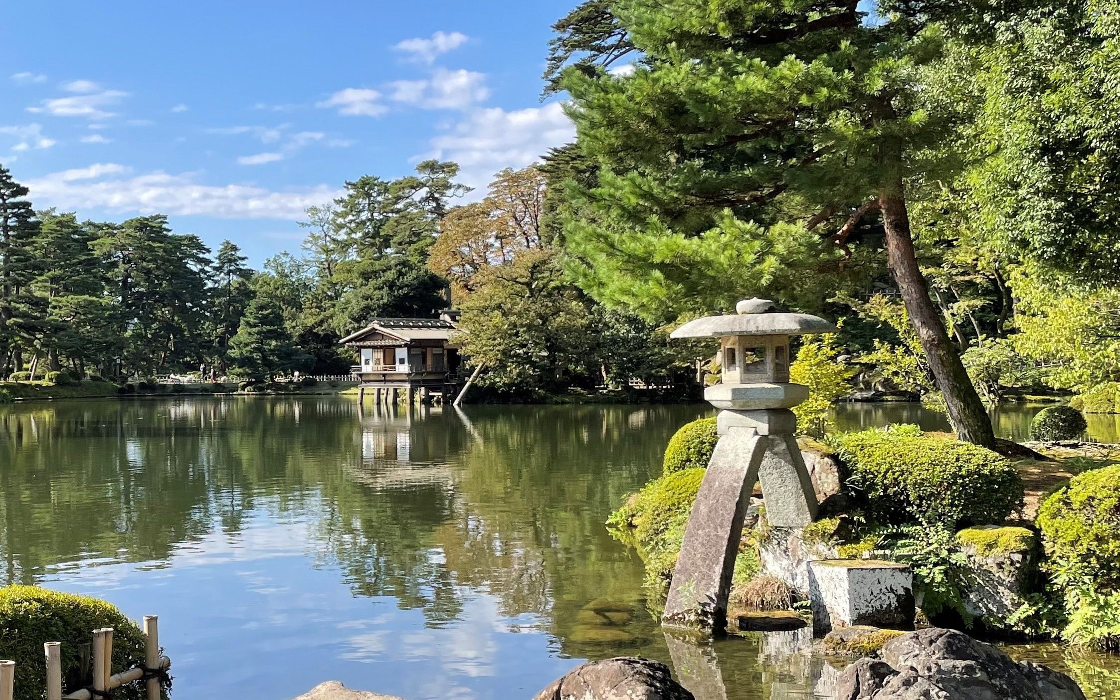 Kenrokuen Garden stone lantern by a tranquil pond with lush greenery in Kanazawa, Japan.