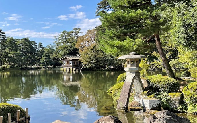 Kenrokuen Garden stone lantern by a tranquil pond with lush greenery in Kanazawa, Japan.