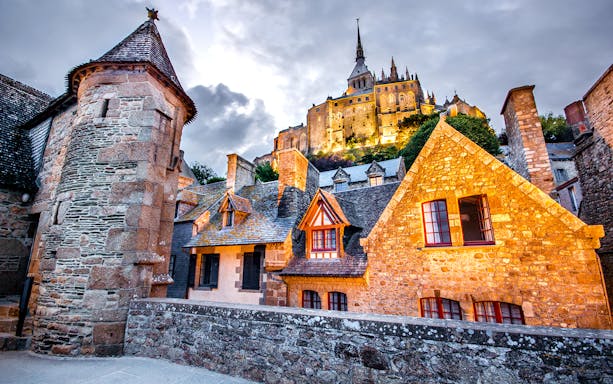 Mont-Saint-Michel Abbey illuminated at night with medieval architecture in the foreground.
