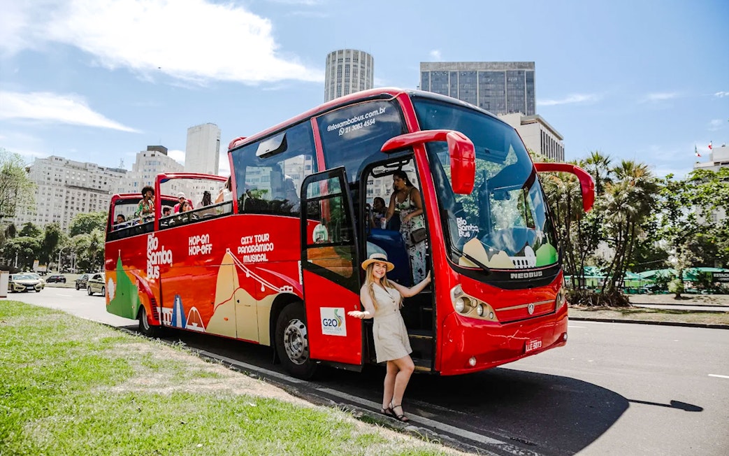 Red Rio de Janeiro hop-on hop-off bus with tourists boarding near city buildings.