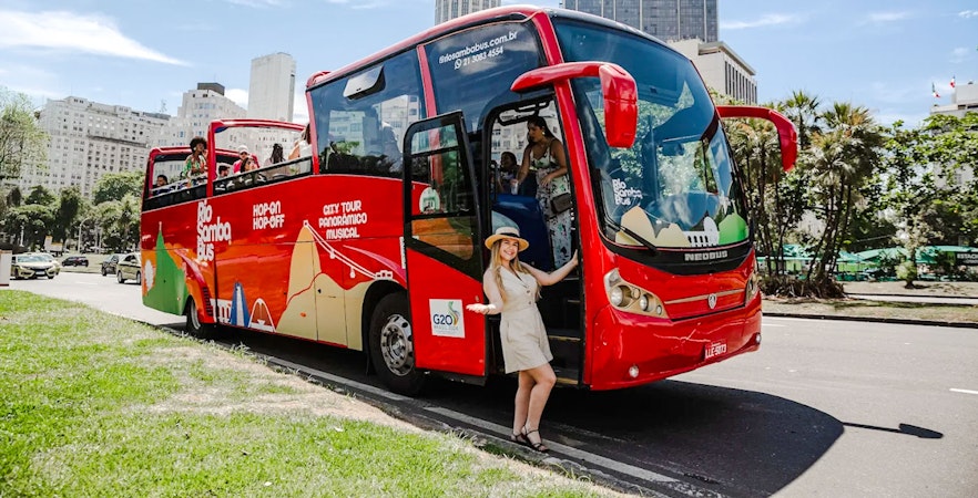 Red Rio de Janeiro hop-on hop-off bus with tourists boarding near city buildings.