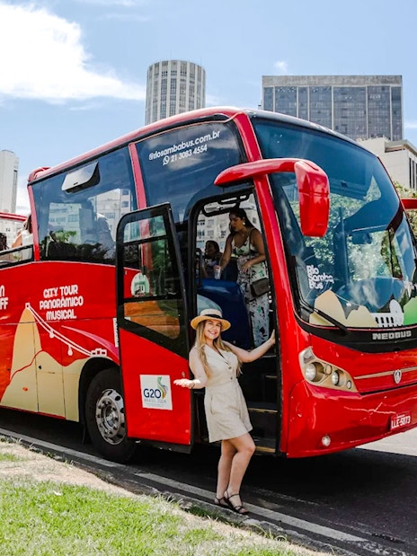 Red Rio de Janeiro hop-on hop-off bus with tourists boarding near city buildings.
