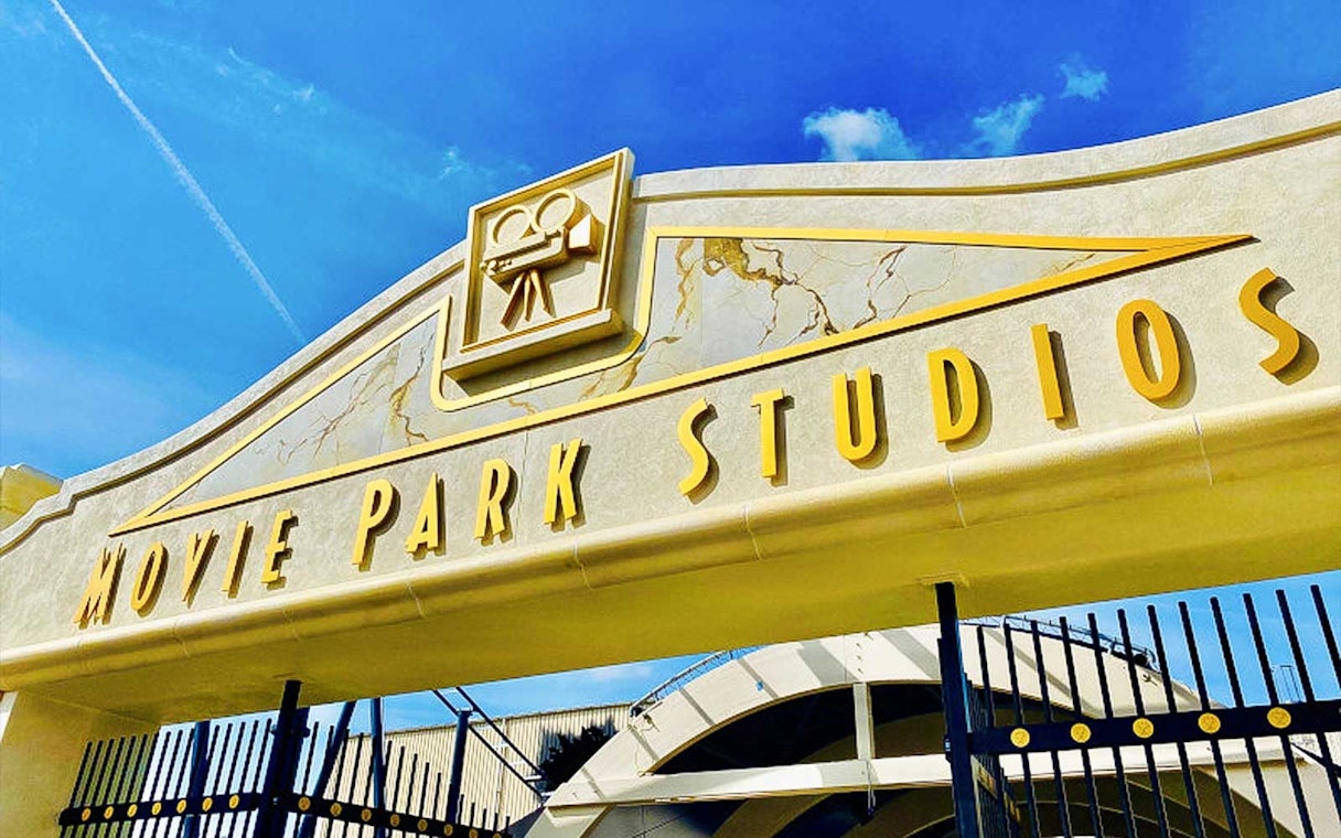 Movie Park Studios entrance gate with film camera icon under blue sky.