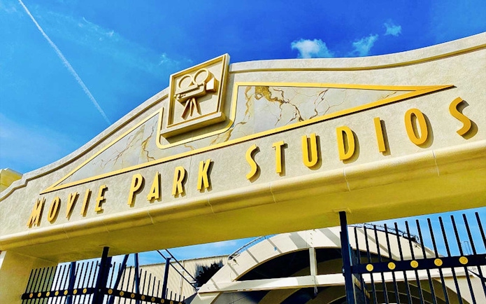 Movie Park Studios entrance gate with film camera icon under blue sky.