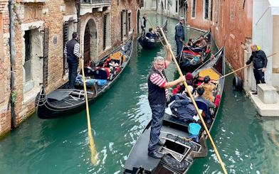 Gondoliers navigating gondolas through a narrow canal in Venice.