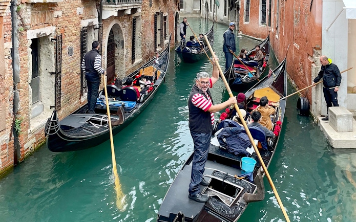 Gondoliers navigating gondolas through a narrow canal in Venice.
