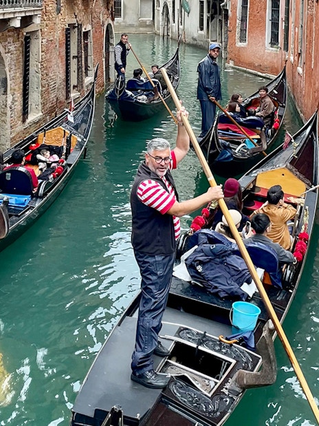 Gondoliers navigating gondolas through a narrow canal in Venice.