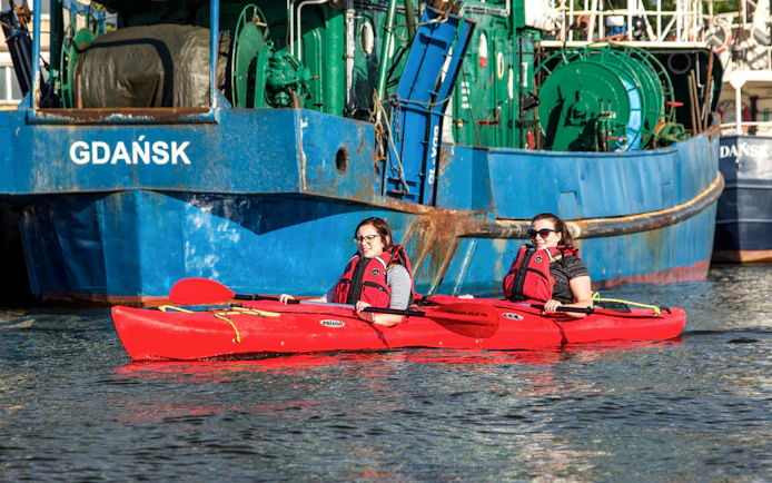 Two people kayaking near a ship in Gdańsk during a private tour.