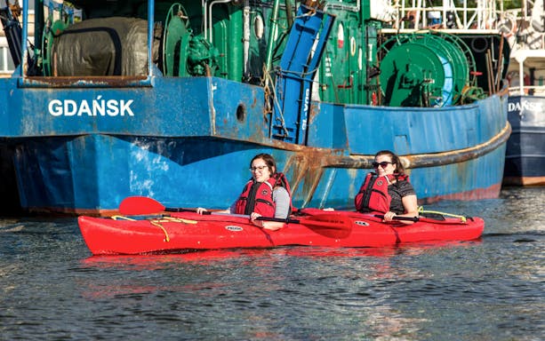 Two people kayaking near a ship in Gdańsk during a private tour.