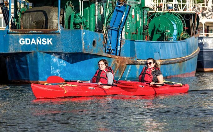 Two people kayaking near a ship in Gdańsk during a private tour.