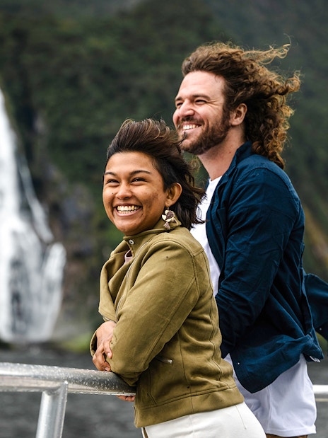 Couple enjoying Milford Sound cruise from viewing deck with waterfall in background.