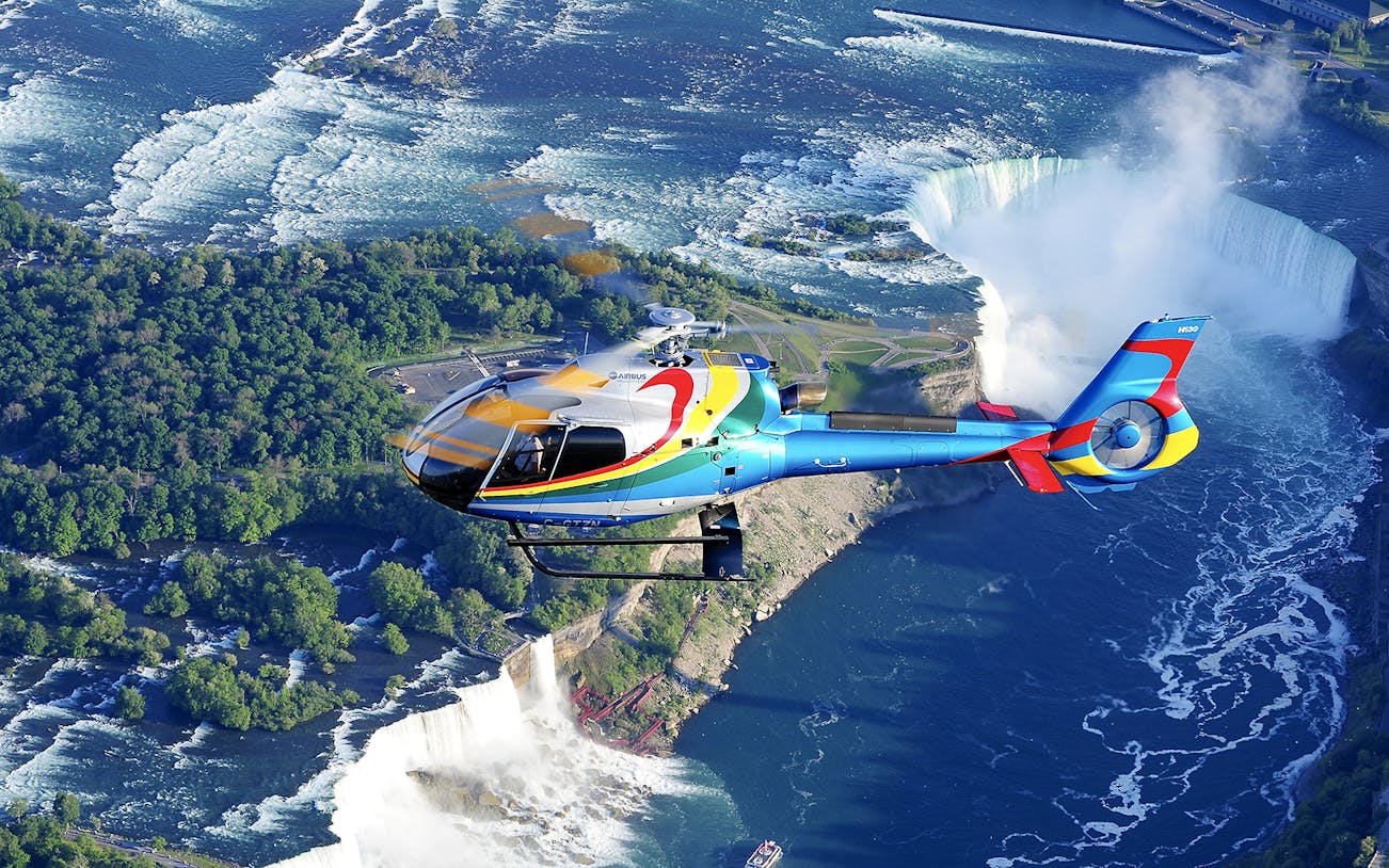 Helicopter flying over Niagara Falls with a view of the waterfalls and surrounding landscape.