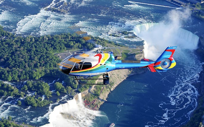 Helicopter flying over Niagara Falls with a view of the waterfalls and surrounding landscape.